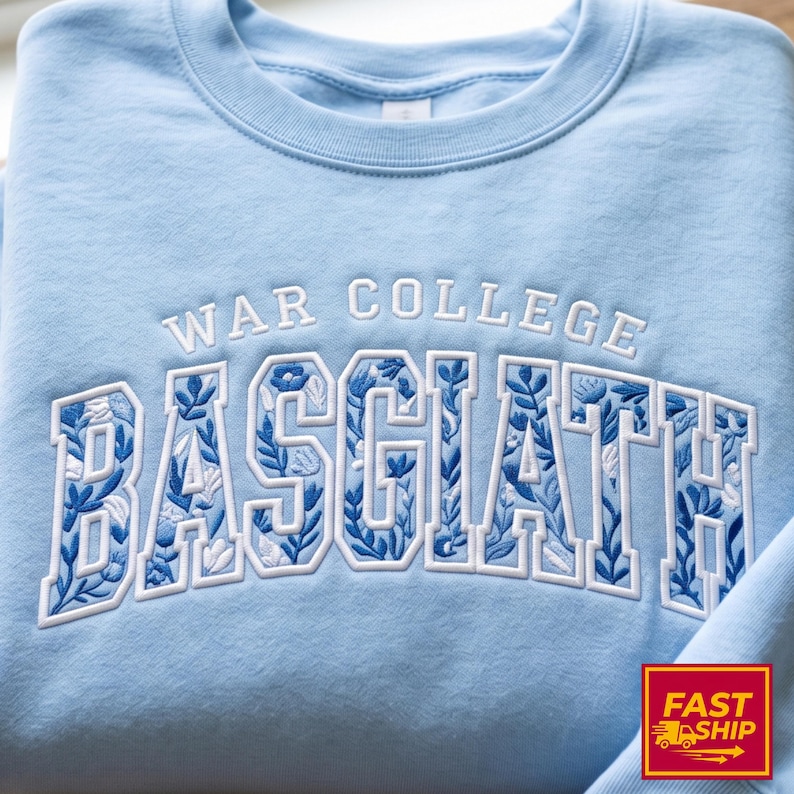 Puede incluir: Sudadera azul claro con las palabras "WAR COLLEGE BASCIATH" bordadas en blanco. Las letras de "BASCIATH" est&aacute;n rellenas con un dise&ntilde;o floral azul. La sudadera tiene cuello redondo.