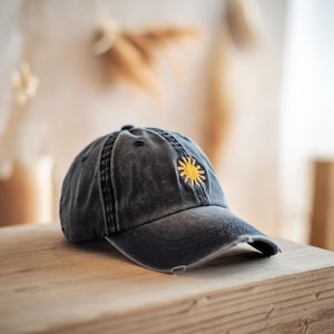 May include: A black denim baseball cap with a yellow embroidered sun design. The cap has a distressed look and a slightly curved brim.