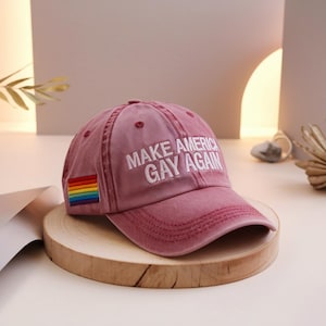 May include: A red baseball cap with the text "Make America Gay Again" embroidered in white. A rainbow pride flag is sewn on the side of the cap.