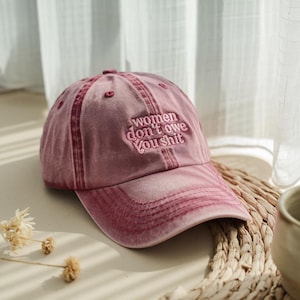 Könnte beinhalten: Eine rosafarbene Baseballkappe mit dem Text "women don't owe you shit", der auf der Vorderseite gestickt ist.