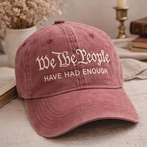 Puede incluir: Gorra de béisbol burdeos con la frase bordada "We The People HAVE HAD ENOUGH" en escritura blanca. La gorra tiene una visera curva y un botón cubierto de tela. El sombrero está hecho de un material suave y desgastado.