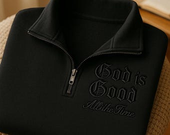 Könnte beinhalten: Schwarzes Sweatshirt mit einem Kragen mit Reißverschluss. Der gestickte Text "God is Good All the Time" ist auf der Vorderseite zu sehen. Das Sweatshirt liegt gefaltet auf einer neutralen Oberfläche.