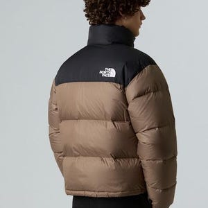 Puede incluir: Chaqueta acolchada marr&oacute;n y negra con cuello alto. La chaqueta tiene una secci&oacute;n superior negra y una secci&oacute;n inferior marr&oacute;n. El logotipo de The North Face es visible en la parte superior izquierda del pecho. La chaqueta la lleva una persona.