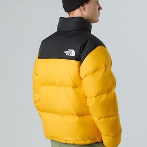 Puede incluir: Un gorro negro y una chaqueta acolchada amarilla y negra. La chaqueta tiene un cuello alto y el logotipo de la marca en el pecho. El modelo lleva pantalones verdes. La chaqueta es una prenda de abrigo c&aacute;lida e informal.