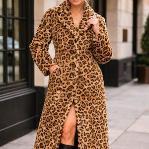 Könnte beinhalten: Ein langer Mantel mit Leopardenmuster in Braun- und Beigetönen. Der Mantel hat einen breiten Kragen und einen Oberschenkelschlitz. Das Model trägt schwarze kniehohe Stiefel. Ein stilvoller Mantel für den Winter.
