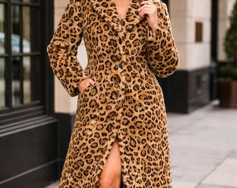 May include: A long, button-down leopard print coat in shades of brown and tan. The coat features a wide collar and a thigh-high slit. The model is wearing black knee-high boots. The coat is a stylish outerwear option.
