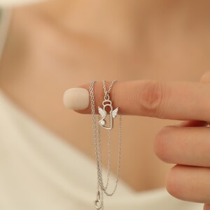 Op de afbeelding: Een zilveren ketting met een engel hanger. De hanger heeft een halo, vleugels en een kleine edelsteen. De ketting wordt getoond tegen een wazige achtergrond.