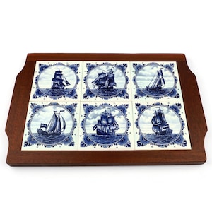 May include: A wooden serving tray with six square ceramic tiles. Each tile features a blue and white illustration of a sailing ship on the sea. The tiles are set in a dark brown wooden frame with handles.
