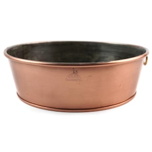 Puede incluir: Un cuenco ovalado de color cobre con interior oscuro. El cuenco tiene un borde redondeado y un cuerpo ligeramente ensanchado. El número "15" y el texto "NRAB KUNGSOR" están estampados en el lateral. Un pequeño asa es visible en el lado derecho.