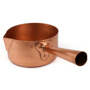 May include: A copper saucepan with a long, tubular handle. The pan has a rounded body with a pouring spout on one side. The handle is attached with rivets. The copper has a warm, reddish-brown color.