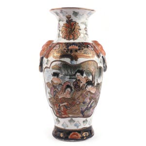 Könnte beinhalten: Eine weiße Keramikvase mit einer handbemalten Szene von Figuren in traditioneller Kleidung in einem zentralen Feld. Die Vase ist mit komplizierten goldenen, orangefarbenen und blauen Blumen- und geometrischen Mustern verziert und hat zwei Griffe.