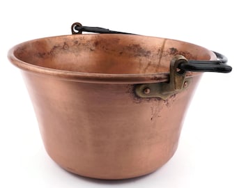May include: A copper bucket with a rounded body and a flared rim. It features a black handle and brass-coloured brackets. The copper has a warm, reddish-brown hue, with some areas showing a darker patina.