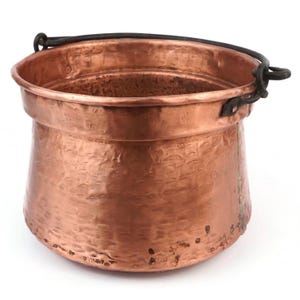 Puede incluir: Una olla de cobre martillado con un asa de metal oscuro. La olla tiene una base redondeada y un borde ligeramente ensanchado. El cobre tiene un color marrón rojizo cálido y una superficie texturizada. El asa está sujeta con remaches.