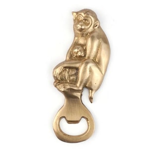 May include: A brass bottle opener shaped like a monkey and baby. The monkey is seated, with the baby monkey in its arms. The bottle opener is at the base. The colour is a warm gold.