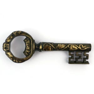 May include: An antique-style key with a bottle opener design. The key is made of metal with a bronze and gold finish. The word "VERITAS" is inscribed on the key's head. The key's handle and key bit feature ornate floral patterns.