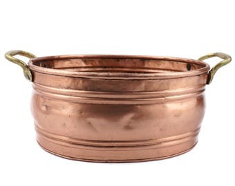 May include: A copper bowl with brass handles. The round bowl has a wide opening and a curved body. The exterior features horizontal bands. The handles are attached to the sides. The bowl is likely for decorative or functional use. The diameter is approximately 25 cm.
