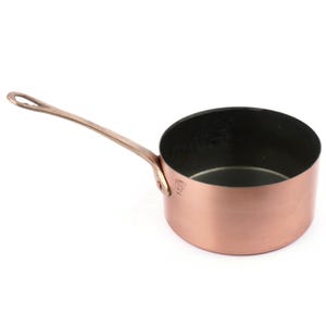 Puede incluir: Una cacerola de cobre con un mango largo. El interior de la cacerola es oscuro, contrastando con el exterior de cobre brillante. El mango está sujeto con remaches. Esta batería de cocina es ideal para cocinar salsas y porciones pequeñas.