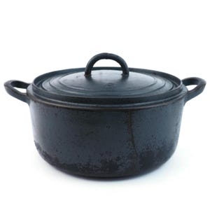 Könnte beinhalten: Ein dunkelgrauer gusseiserner Dutch Oven mit passendem Deckel. Der Topf hat zwei seitliche Griffe und einen Schlaufengriff am Deckel. Das Äußere hat ein strukturiertes, gesprenkeltes Aussehen, das eine rustikale oder Vintage-Ästhetik suggeriert. Zum Kochen.