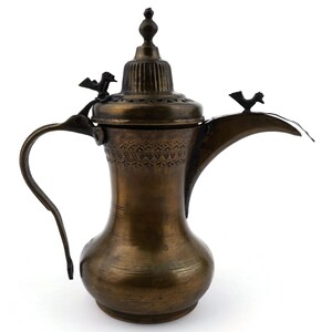 Könnte beinhalten: Eine bronzefarbene Kaffeekanne mit gebogenem Griff und Ausguss. Die Kanne hat dekorative Ätzungen und zwei kleine vogelartige Akzente. Der Deckel ist gerippt und mit einer kleinen Spitze versehen.