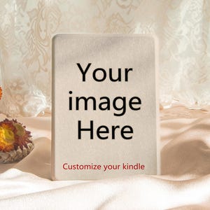 Könnte beinhalten: Eine rechteckige, cremefarbene Kindle-Hülle mit dem Text "Your image Here" in Schwarz und "Customize your kindle" in Rot. Die Hülle befindet sich vor einem Hintergrund aus weichem, drapiertem Stoff und Trockenblumen.