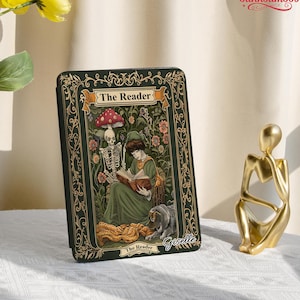 May include: A dark green tarot card with the title "The Reader" features a woman reading a book, a skeleton, and a dog. The card has a decorative border and the name "Giselle" is written on the bottom right.