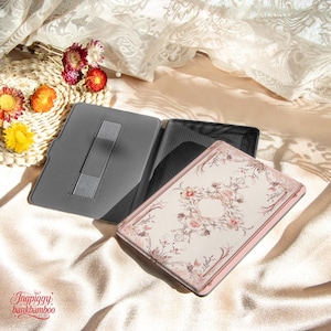 Puede incluir: Una funda gris para tableta con soporte y dise&ntilde;o floral. La funda est&aacute; abierta, revelando el interior y una tableta con un patr&oacute;n floral rosa y crema. La funda est&aacute; sobre una superficie satinada.