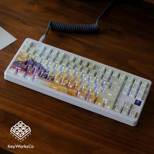 May include: A white mechanical keyboard with illuminated keys and a custom keycap design showing an abstract landscape. It has a coiled grey cable. The KeyWorksCo logo is visible.