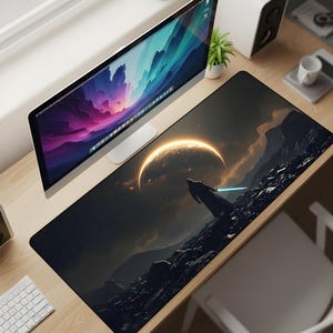 Puede incluir: Alfombrilla de escritorio negra y gris con una escena de ciencia ficción. Una silueta sostiene un sable de luz azul sobre un fondo de una luna creciente brillante y terreno rocoso. Se ven un monitor de ordenador, un teclado y otros accesorios de escritorio.