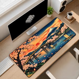 May include: A rectangular desk mat featuring a vibrant illustration of a landscape with a snow-capped mountain, a wooden bridge over water, small boats, and blooming cherry blossom trees under a bright orange and yellow sunset sky.