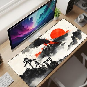 May include: A rectangular desk mat featuring a Japanese-inspired landscape design. The artwork depicts a red sun, a volcano, and traditional Japanese structures in shades of black, white, and red. The mat is designed to protect the desk surface.