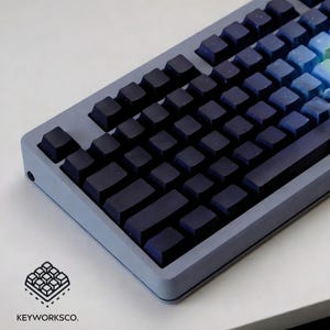 May include: A close-up of a mechanical keyboard with dark blue keycaps and a gradient of blue and green keys on the right side. The keyboard has a light gray frame. The logo "KEYWORKSCO." is in the bottom left corner.