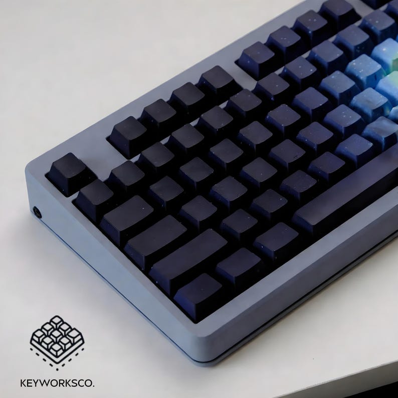 May include: A close-up of a mechanical keyboard with dark blue keycaps and a gradient of blue and green keys on the right side. The keyboard has a light gray frame. The logo "KEYWORKSCO." is in the bottom left corner.