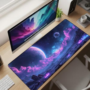 May include: A large rectangular desk mat featuring a vibrant space scene with a large planet, purple clouds, and a ringed planet. The mat has a black border and is placed on a wooden desk with a computer monitor and keyboard.