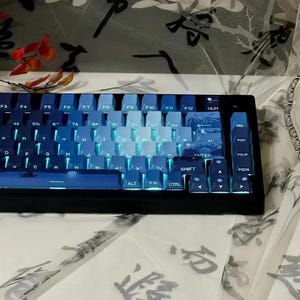 May include: A blue and black mechanical keyboard with a gradient color scheme on the keys. The keyboard has a number pad, function keys, and arrow keys. The keys are backlit with a blue light.