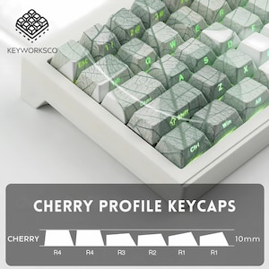 K&ouml;nnte beinhalten: Wei&szlig;e mechanische Tastatur mit grauen und wei&szlig;en Tastenkappen. Die Tastenkappen haben ein Holzmaserungsdesign und gr&uuml;ne Schrift. Der Text "CHERRY PROFILE KEYCAPS" wird darunter angezeigt. Die Tastatur ist 1 cm hoch.