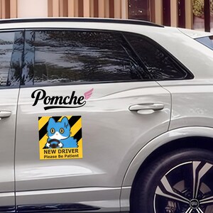 May include: A white car with a "Pomche" decal and a "New Driver Please Be Patient" magnet. The magnet shows a blue cat driving a car on a yellow background with black diagonal stripes.