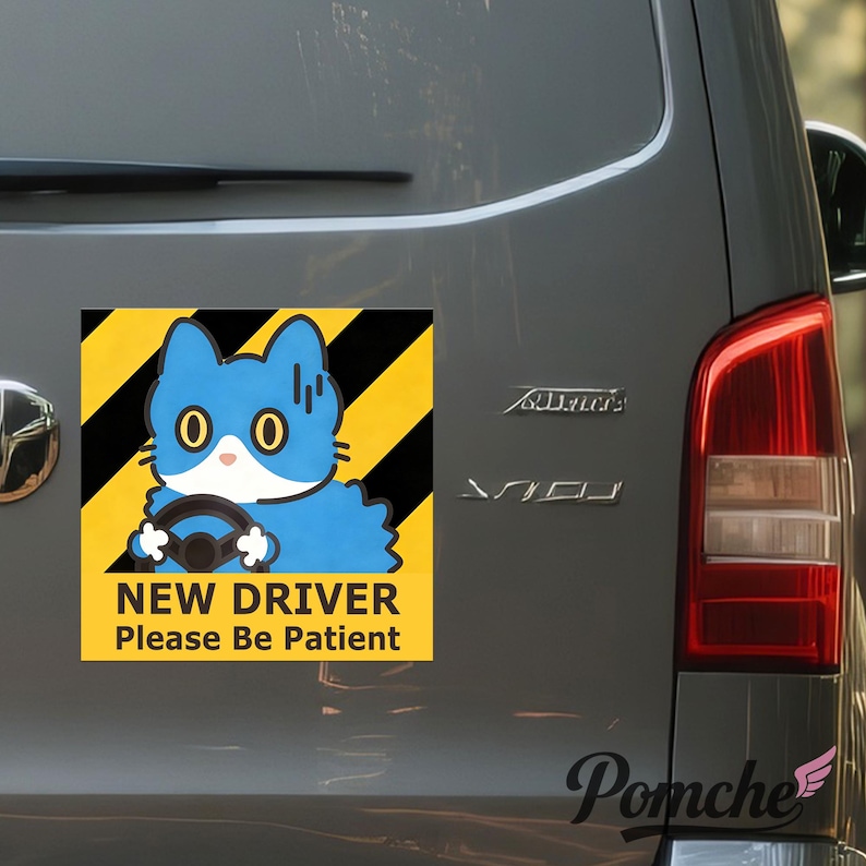May include: A yellow and black hazard sticker featuring a blue cartoon cat driving. The sticker reads "NEW DRIVER Please Be Patient". The sticker is attached to the rear of a grey vehicle.