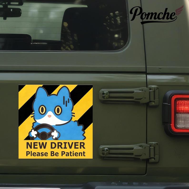 May include: A square sticker featuring a blue cartoon cat driving, set against a yellow and black striped background. The text "NEW DRIVER Please Be Patient" is below the cat. The sticker is attached to a green vehicle.