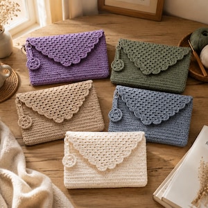 May include: Five rectangular crochet envelope clutches in purple, olive green, beige, blue, and cream. Each clutch features a scalloped flap, a solid body, and a small circular charm attached to the side. The items are arranged in a group.