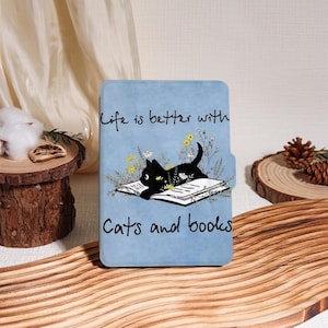 Könnte beinhalten: Hellblaue E-Reader-Hülle mit einer Illustration einer schwarzen Katze auf einem offenen Buch mit Blumen. Der Text lautet "Life is better with Cats and books".