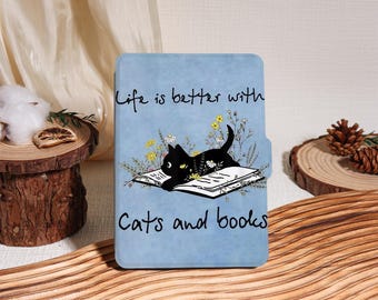 Może przedstawiać: Jasnoniebieskie etui na czytnik e-booków z czarnym kotem leżącym na otwartej książce z kwiatami. Na etui widnieje napis "Life is better with Cats and books".