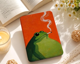 Może przedstawiać: Prostokątne etui na czytnik e-booków z ilustracją w stylu obrazu olejnego przedstawiającą zieloną żabę z dużymi czarnymi oczami palącą papierosa, na tle żywego pomarańczowego tła z cienką smugą białego dymu unoszącą się z papierosa.
