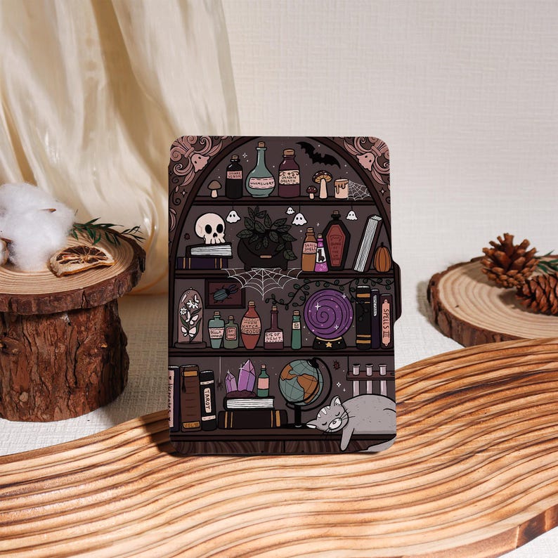 May include: A decorative tablet case featuring a whimsical illustration of a witch's shelf. The design includes potion bottles, a skull, a crystal ball, and a sleeping gray cat. The color palette is primarily dark purple, brown, and gray.