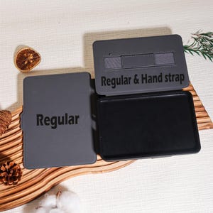 May include: A gray tablet case with the text "Regular" on the front cover and "Regular & Hand strap" on the inside cover. The case is open, revealing a black interior. The case is designed to protect a tablet.