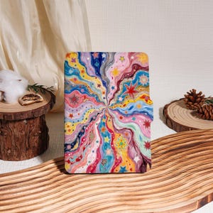 May include: A rectangular case with a vibrant, colourful abstract design featuring radiating lines and stars in shades of pink, blue, yellow, and purple. The case is likely for a phone or tablet.