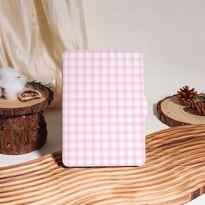 Op de afbeelding: Een tablet hoesje met een roze en wit ruitpatroon. De hoes heeft een rechthoekige vorm met afgeronde hoeken en een magnetische sluiting. De achtergrond bevat houten elementen en decoratieve accenten.