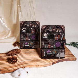 May include: Two decorative cases with a witchy bookshelf design. The cases feature a dark gray background with shelves filled with potion bottles, skulls, and a sleeping cat. The cases are placed on a wooden cutting board.