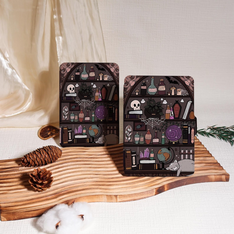 May include: Two decorative cases with a witchy bookshelf design. The cases feature a dark gray background with shelves filled with potion bottles, skulls, and a sleeping cat. The cases are placed on a wooden cutting board.