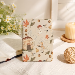 May include: A rectangular e-reader case featuring a cream-colored background with a repeating pattern of autumn-themed illustrations, including a fox wearing an apron, a mouse with a mushroom hat, maple leaves, acorns, birds, and a mushroom house.