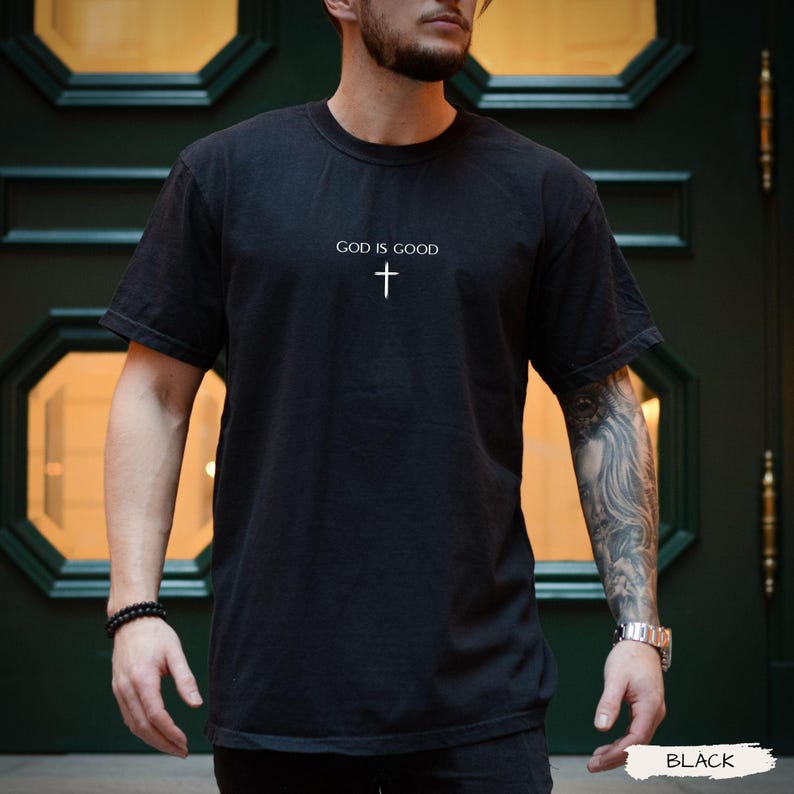 Peut inclure: T-shirt noir avec l'inscription "GOD IS GOOD" surmontant une croix blanche. Le t-shirt &agrave; manches courtes est fait d'une mati&egrave;re douce. Le mot "BLACK" est imprim&eacute; en bas &agrave; droite de l'image.
